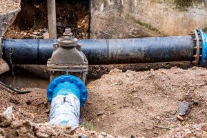Large black and blue underground water pipes with valve joints are exposed in a dirt trench, possibly for maintenance or repair work by Impact Plumbing, leading providers of plumbing services in Las Vegas NV.