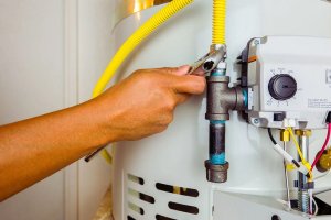 A person’s hand uses a wrench to tighten a pipe on a water heater, with visible yellow gas tubing and control panel components—showcasing expert Plumbing Services from Impact Plumbing in Las Vegas NV.