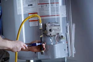 A person uses a wrench to tighten a gas line connection on a water heater in Las Vegas NV, with safety instructions visible—demonstrating expert Plumbing Services from Impact Plumbing.