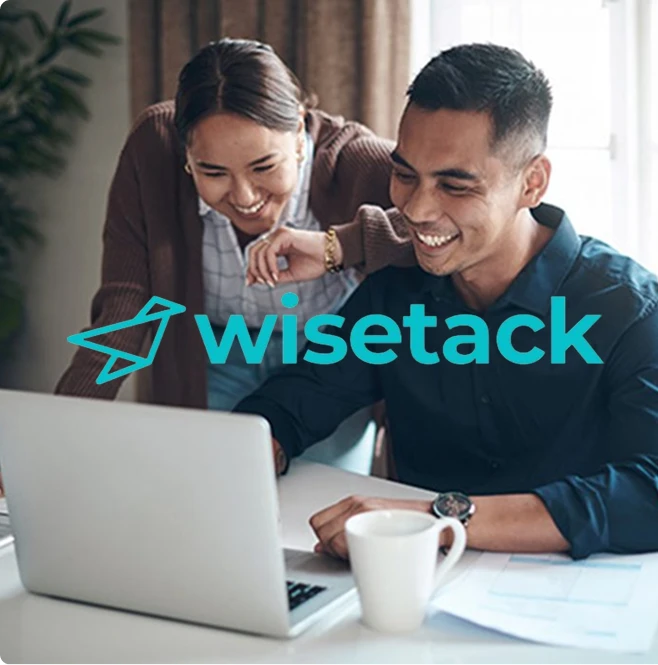 Two people smiling and working together at a laptop, with papers and a coffee mug on the table. The word wisetack and a paper airplane logo are overlaid, highlighting Impact Plumbing’s services in Las Vegas NV.