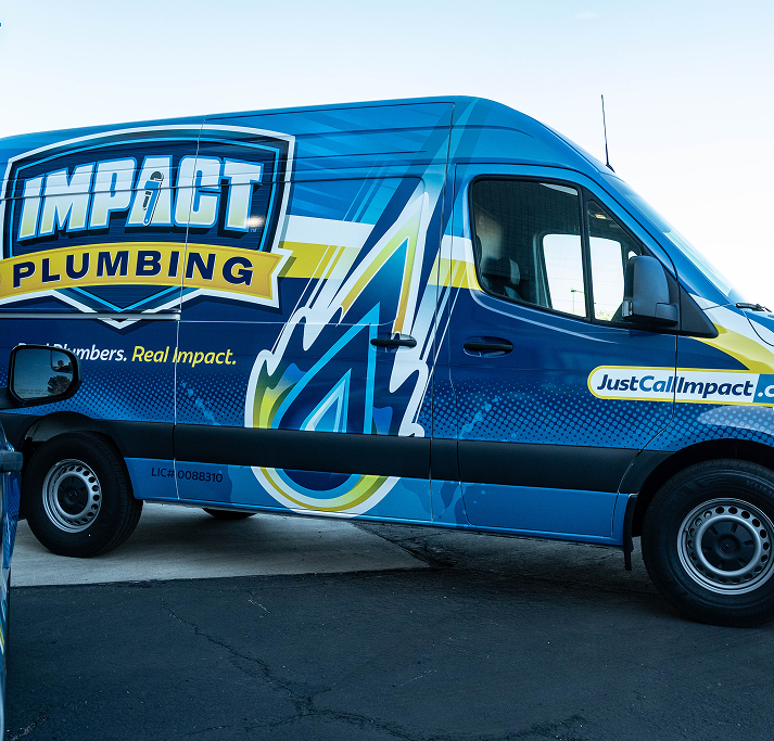 A blue Impact Plumbing van with bold branding is parked on a street in Las Vegas NV. The van promotes expert plumbing services, the slogan “Real Plumbers. Real Impact.” and the website JustCallImpact.com on its side.